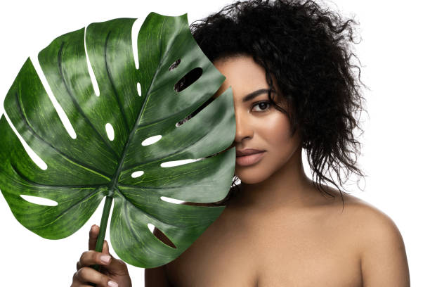 hermosa mujer negra con una piel suave que sostiene la hoja tropical verde - facial expression isolated lifestyles exoticism fotografías e imágenes de stock