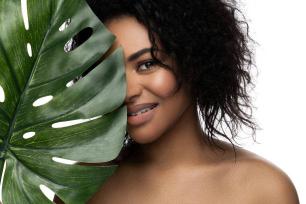 belle femme noire avec une peau lisse tenant une feuille tropicale verte - facial expression isolated lifestyles exoticism photos et images de collection