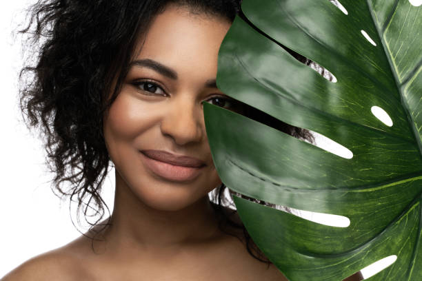 hermosa mujer negra con una piel suave que sostiene la hoja tropical verde - facial expression isolated lifestyles exoticism fotografías e imágenes de stock