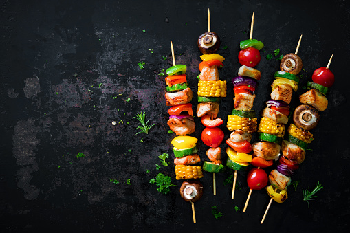 Chicken kebabs on skewers with mushrooms and vegetables on dark background