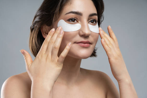 Beautiful woman with a smooth skin applying adhesive under-eyes patches for dark circles Beautiful brunette woman with a smooth skin applying adhesive under-eyes patches for dark circles one eyed stock pictures, royalty-free photos & images