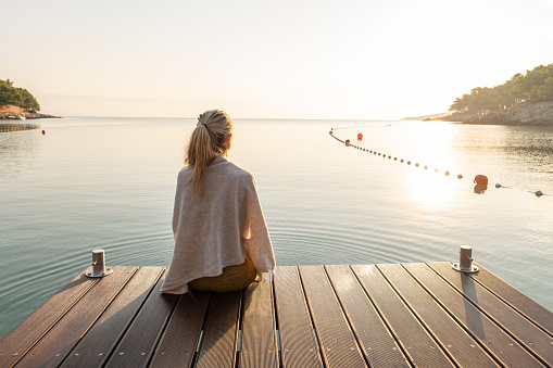 Young woman relaxing on pier at sunrise enjoying the sea view