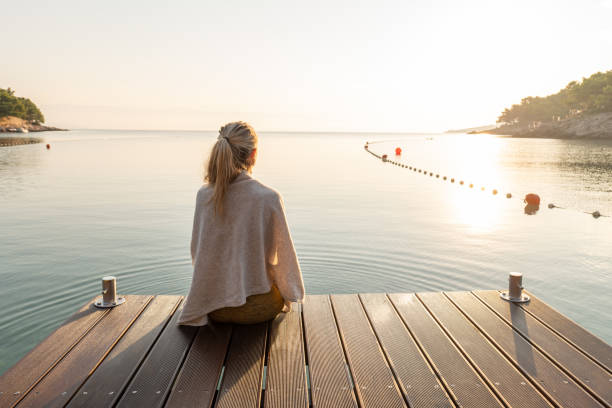 młoda kobieta relaksująca się na molo o wschodzie słońca, podziwiając widok na morze - jetty zdjęcia i obrazy z banku zdjęć