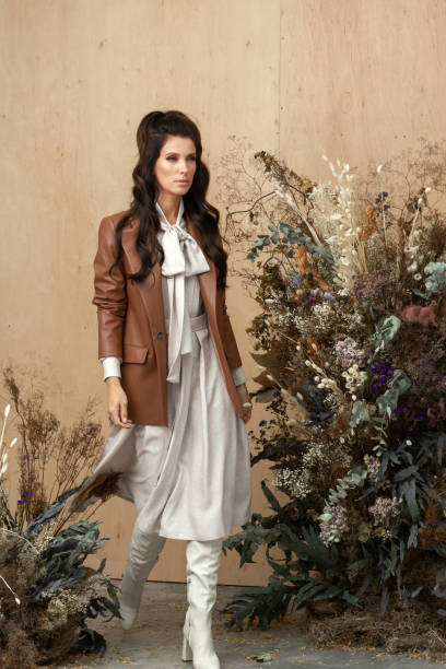 Studio autumn fashion portrait of beautiful confident woman with long brown hair wearing stylish trendy clothes in earth tones. Autumn hairstyles and make up trend concept. retrato de moda de otoño de estudio de hermosa mujer segura de sí misma con cabello largo castaño con ropa elegante y moderna en tonos tierra y posando sobre fondo de madera decorado con flores secas. concepto de peinados otoñales y maquillaje de tende
