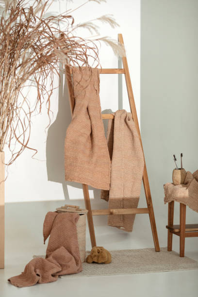 Natural waffle linen towels in earth tones on wood bench and towel ladder with bamboo toothbrushes, rattan baskets, and soap dispenser. Daily body care, spa and wellness zero waste bathroom concept toallas de lino de gofre natural en tonos tierra sobre banco de madera y escalera de toallas con cepillos de dientes de bambú, cestas de ratán y dispensador de jabón. concepto de baño diario para el cuidado del cuerpo, spa y bienestar cero residuos