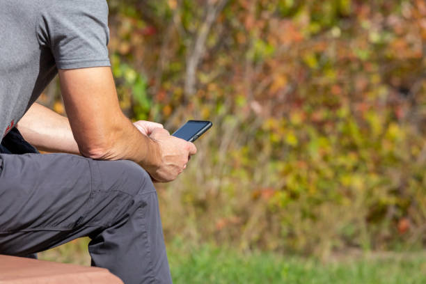 Man Holding Phone While Sitting on Bench Outdoors stock photo