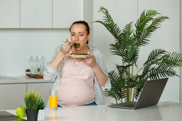 istock Black haired pregnant lady drinks and eats with appetite 1344431372