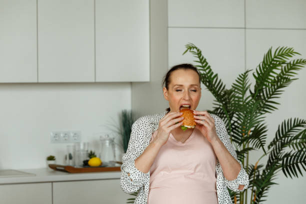 istock Pregnant lady eats burger with satisfaction sitting at table 1344431388