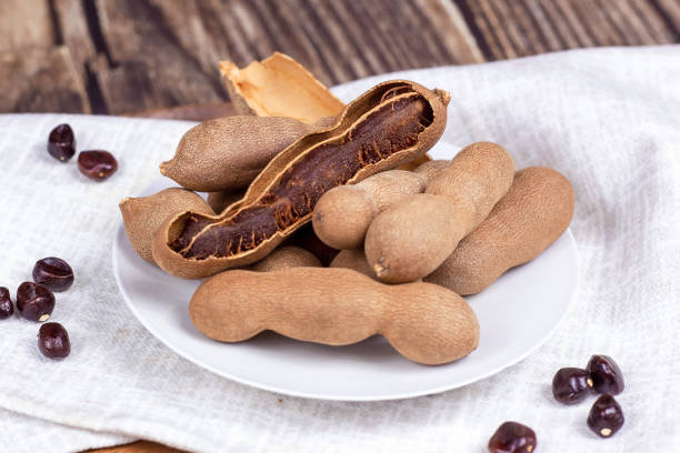 istock Fresh brown tamarind fruit pods ripe with seeds on light textile background close up 1344434890