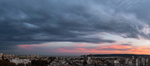 Stormy gray clouds is coming to seaside city at sunset. Panorama. Stormy gray clouds is coming to seaside city at sunset. Panorama of dramatic overcast sky at evening. Dark stratus clouds hang over Varna, Bulgaria. Weather change concept. Storm is coming wide landscape. stratus clouds stock pictures, royalty-free photos & images