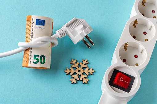 White electric plug tied to a knot on a fifty euro banknotes, snowflake and power strip over blue background. Rise in electricity prices in the cold season. Increasing of electricity cost concept.