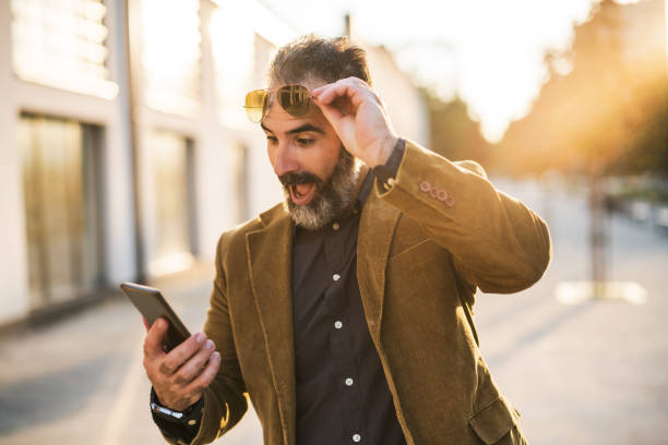 Surprised businessman with beard looking at mobile phone stock photo