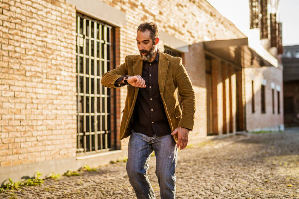 Modern businessman with beard looking at watch and walking in hurry on the street.