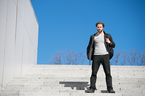 guy on stairs, thoughtful young man sitting on a flight of steps staring into the distance with a serious expression against a blue sky background, guy with sport bag, copy space
