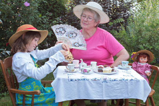 A charming spring garden is a perfect setting for a loving grandmother and her 6 year old granddaughter to have a tea party, accompanied by a vintage doll. Accessories include a lace fan, pretty straw hats, bright pastel dresses, delicate antique china tea cups, cupcakes, and an antique embroidered tablecloth.
