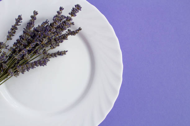 Table setting with the white plate and dried lavender on the purple background. Top view. Copy space.