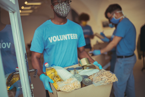 Depicting a scene at the volunteering center where a group of people is helping the society by filling up the boxes with food and home supplies.