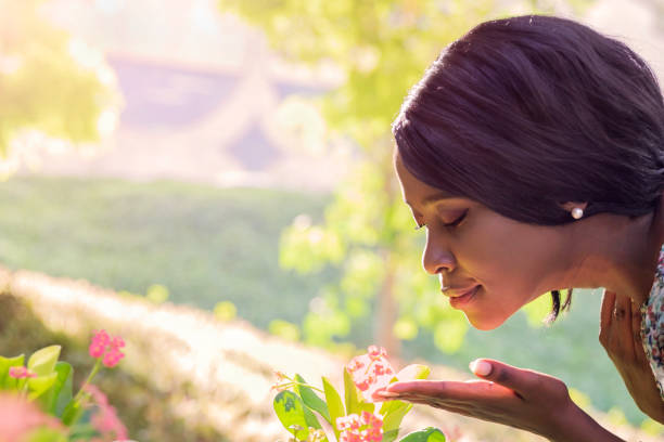African young woman sniffing  flowers in the garden with closed eyes