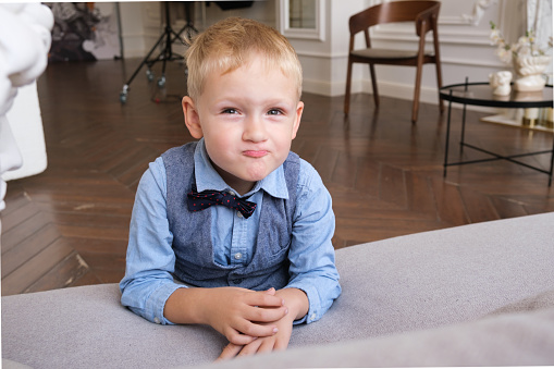 Portrait of a five-year-old blonde boy in a shirt, vest and bow tie. Close-up of the child's face. The boy smiles and makes a face.