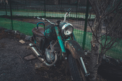 Old rusty motorcycle near fence on ground. Close up of abandoned broken motorbike