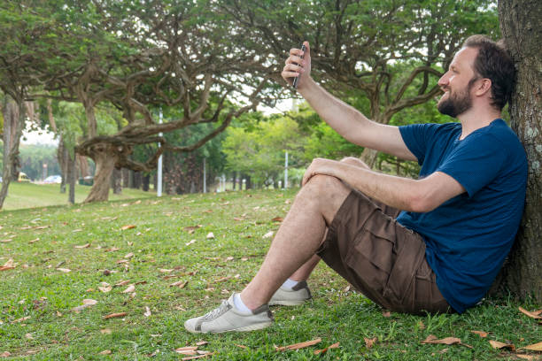 istock Man makes a selfie sitting in the park leaning on a tree 1344461396