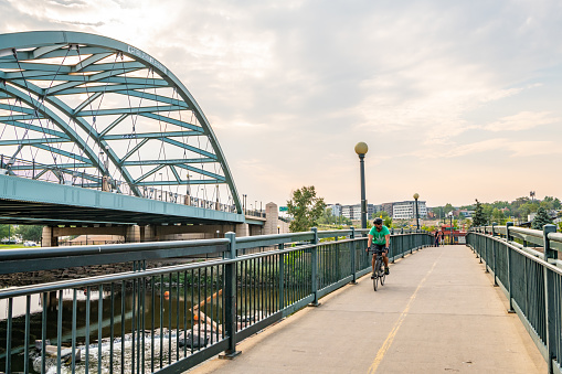 Denver, CO - August 31, 2021: A man riding a bicycle crosses the pedestrian bridge over Colfax Avenue at Confluence Park, in the Highland and River North (RiNo) neighborhoods.