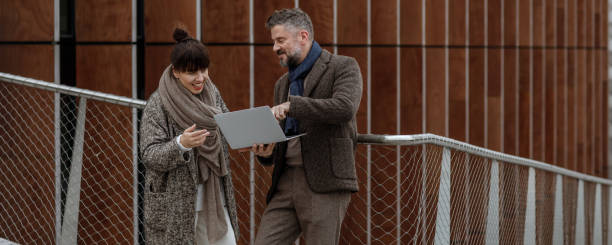 istock Handsome businessman using laptop on a terrace outside office, working. Grey haired man in autumn brown trendy style clothes on terrace in business area. Productive time outside the office 1344465638