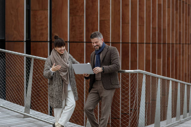 istock Handsome businessman using laptop on a terrace outside office, working. Grey haired man in autumn brown trendy style clothes on terrace in business area. Productive time outside the office 1344465650