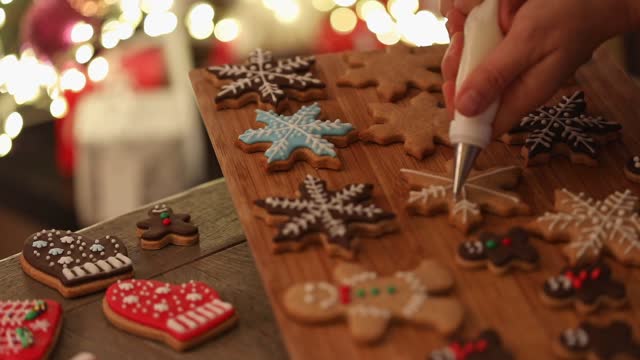 A pair of hands decorating homemade gingerbread shapes with icing ready to send as gifts