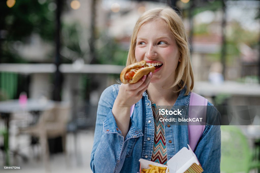 Portrait of young woman eating hot dog A young Caucasian woman is eating a hot dog and enjoying Hot Dog Stock Photo