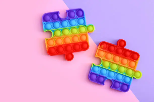 Photo of Popit toy in the form of a puzzles on a colorful background. Multicolored Pop it toy
