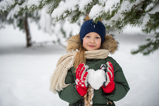Happy child girl plaing with snow on a snowy winter walk. Heart made of snow.