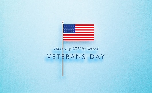 Veteran's Day message next to tiny American flag on blue  background. Horizontal composition with copy space. Directly above. Veteran's Day concept.