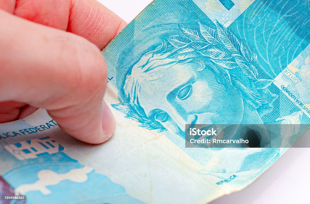 Real - BRL, money from Brazil. A man holding in hand a 100 reais banknote with white background. close up photo. Adult Stock Photo