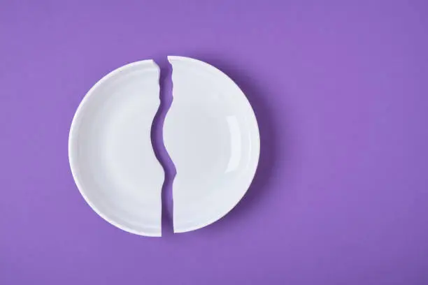 broken white plate on purple background copy space top view