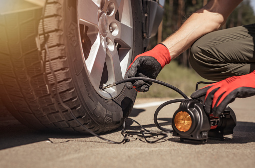 Tire pump inflating car wheel. Tyre inflator in man hands with manometer.