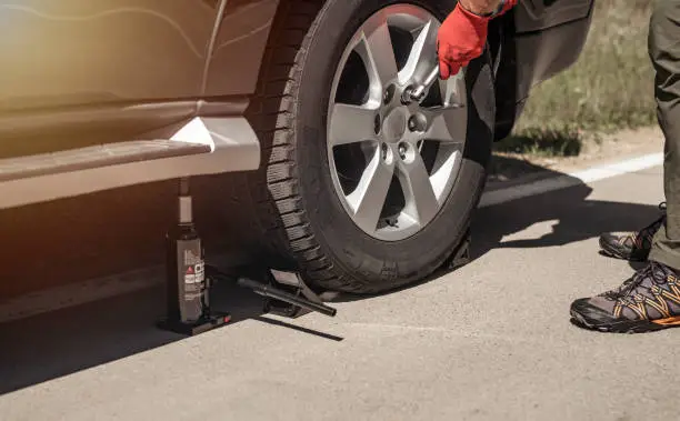 Hydraulic car jack is put under auto by hands in gloves, close up.