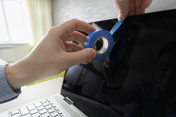 Spying on privacy via webcam. Human hand blocks a webcam of laptop by an adhesive tape. persecution mania, persecution complex, delusion of persecution Human hand blocks a webcam of laptop by an adhesive tape. persecution mania, persecution complex, delusion of persecution. Spying on privacy via webcam. camera covers pictures stock pictures, royalty-free photos & images