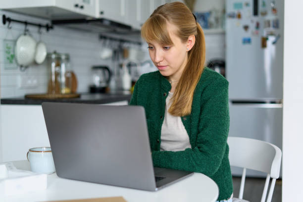 istock Focused female working from kitchen on laptop. Concept of home office and multitasking 1344498921