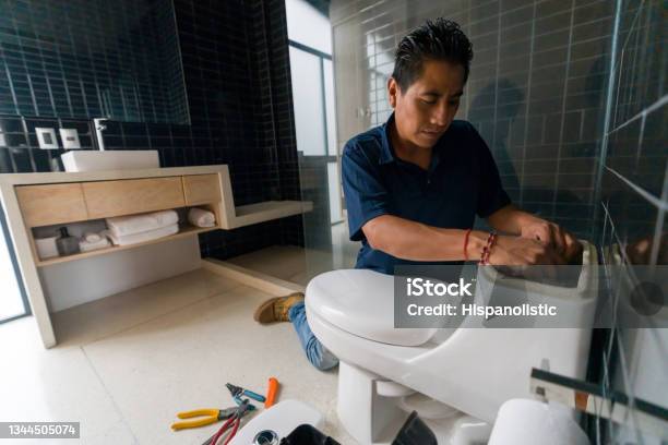 Latin American Plumber Fixing A Toilet In The Bathroom Stock Photo - Download Image Now
