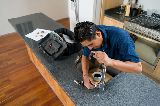 Latin American plumber fixing a problem with the faucet of the sink in the kitchen - home improvement concepts