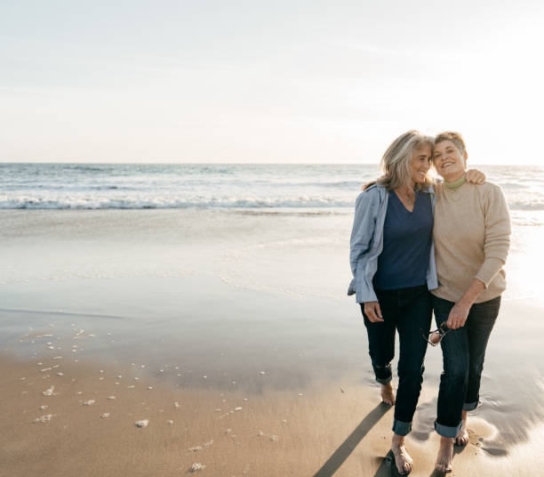 Two beautiful senior woman on their barefoot walk Same-sex couple walking on the beach homosexual couple stock pictures, royalty-free photos & images