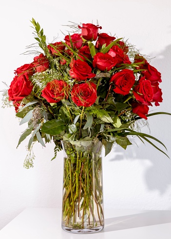 Red roses bouquet in glass vase on white background