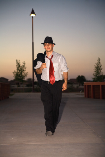 A handsome man in business suit and hat strolling casually in the twilight of the day.