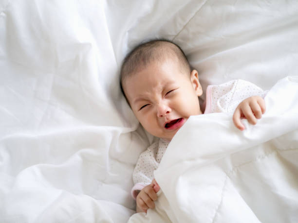 Close up Adorable Asian baby infant girl cry on a white bed , colic symptom or hungry unhappy of infant concept stock photo