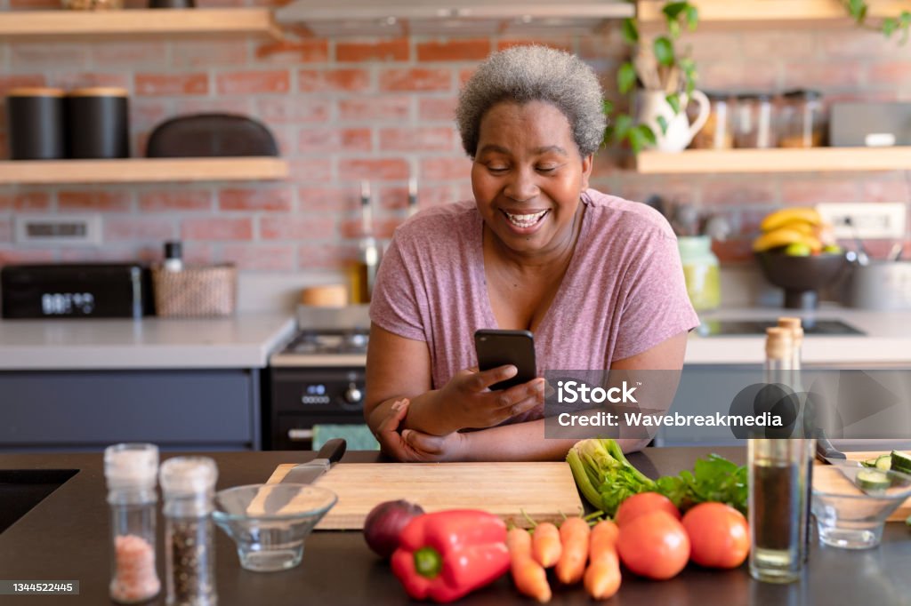 Happy african american senior woman using smartphone it kitchen Happy african american senior woman using smartphone it kitchen. retirement lifestyle, leisure and spending time at home. Women Stock Photo