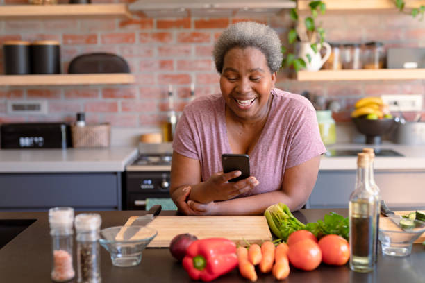 Happy african american senior woman using smartphone it kitchen stock photo