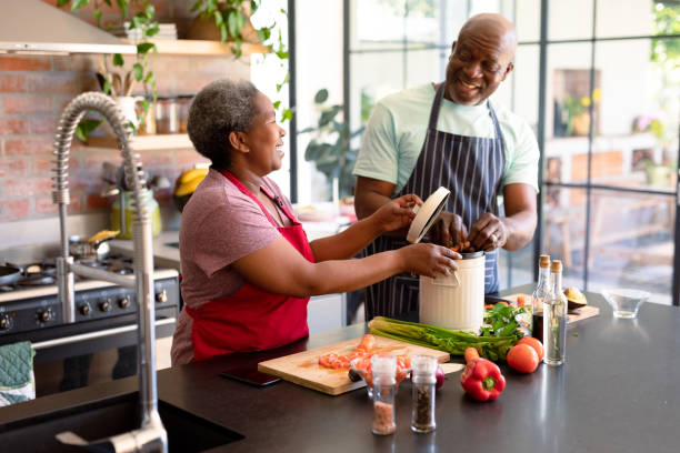 happy african american senior couple cooking together in kitchen - cooking senior adult healthy lifestyle couple imagens e fotografias de stock