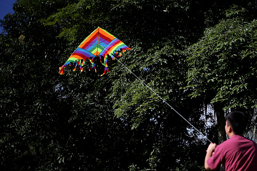 An Asian young man is enjoying kite flying during his leisure time.