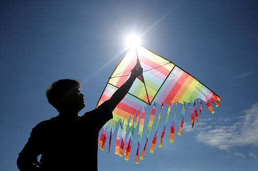An Asian young man is enjoying kite flying during his leisure time.
